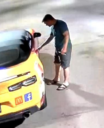 The man standing at the rear of the yellow vehicle, reaching towards it.